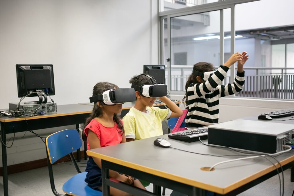 Cute multiethnic kids learning to use virtual reality glasses. Concentrated children sitting at table together and wearing VR headsets in classroom. Informatics, study and education concep