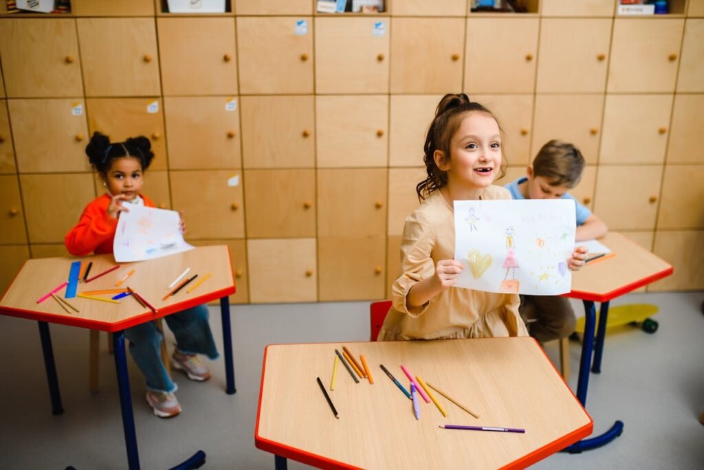 A cheerful little girl proudly displays her colorful drawing in a classroom.