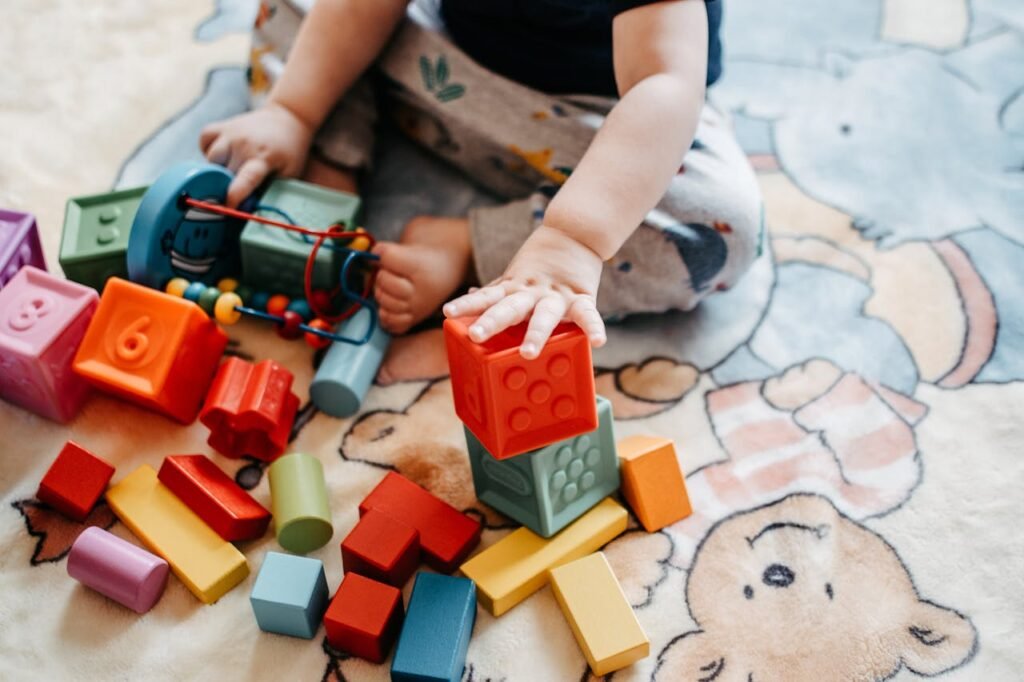 A joyful baby sits on a colorful rug, happily stacking and playing with colorful blocks.