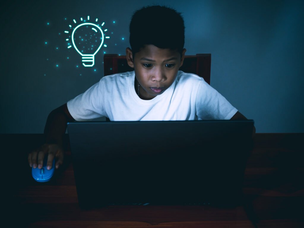 Education concept image. Creative idea and innovation. boy sitting staring at computer and there is a light bulb icon next to it.